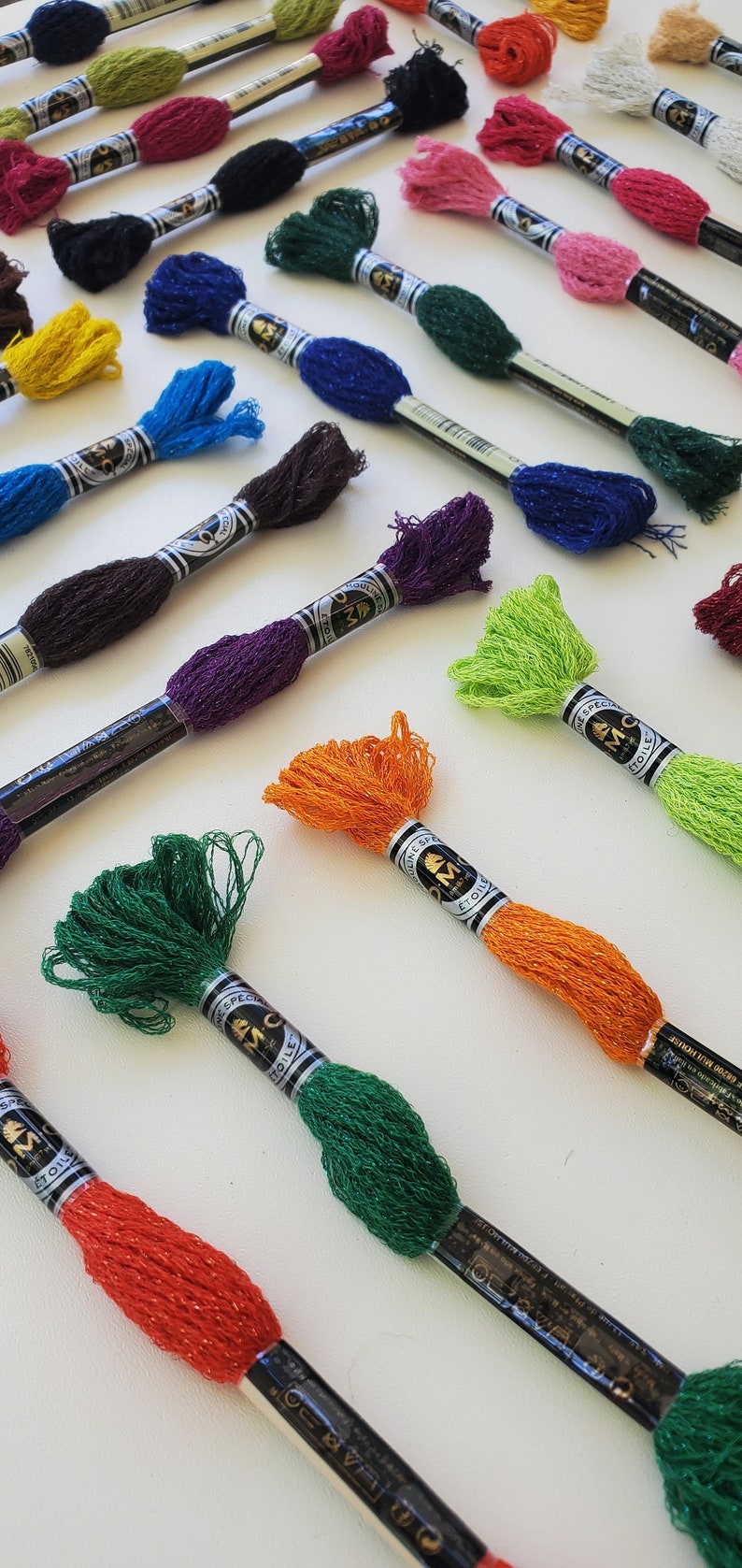 Puede incluir: Surtido de carretes de hilo de bordar DMC en varios colores, incluyendo verde, naranja, rojo, morado y azul. Cada carrete tiene una etiqueta negra con letras doradas que dicen "DMC Special Moulin&eacute; Etoile".