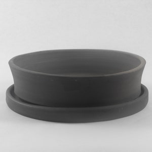 May include: A dark gray ceramic planter with a matching saucer. The planter has a wide, shallow bowl shape with a slightly flared rim.
