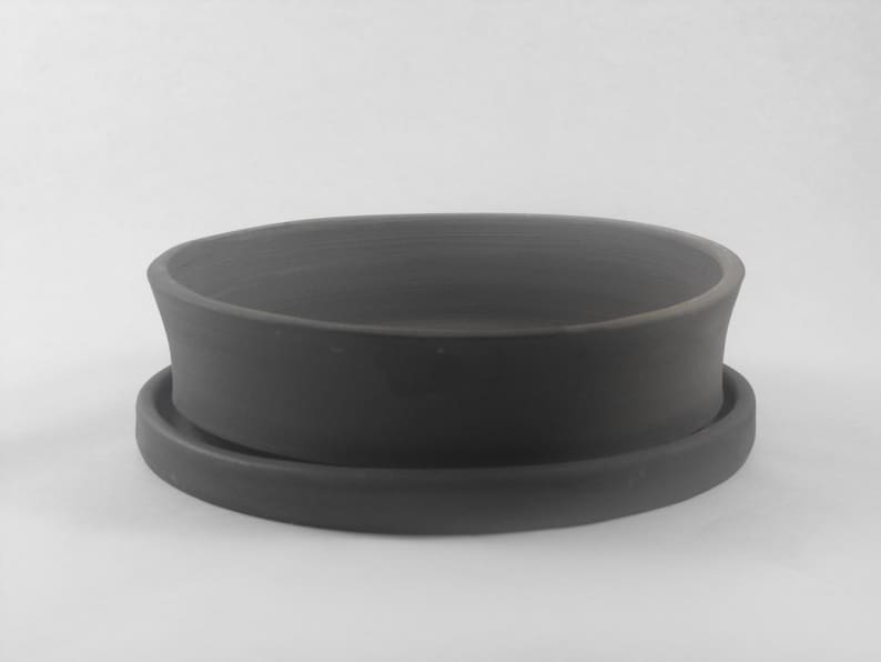 May include: A dark gray ceramic planter with a matching saucer. The planter has a wide, shallow bowl shape with a slightly flared rim.