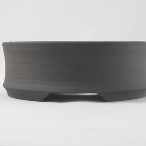 May include: A dark gray ceramic bonsai pot with a rounded base and three small feet.