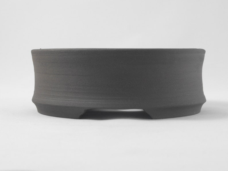 May include: A dark gray ceramic bonsai pot with a rounded base and three small feet.