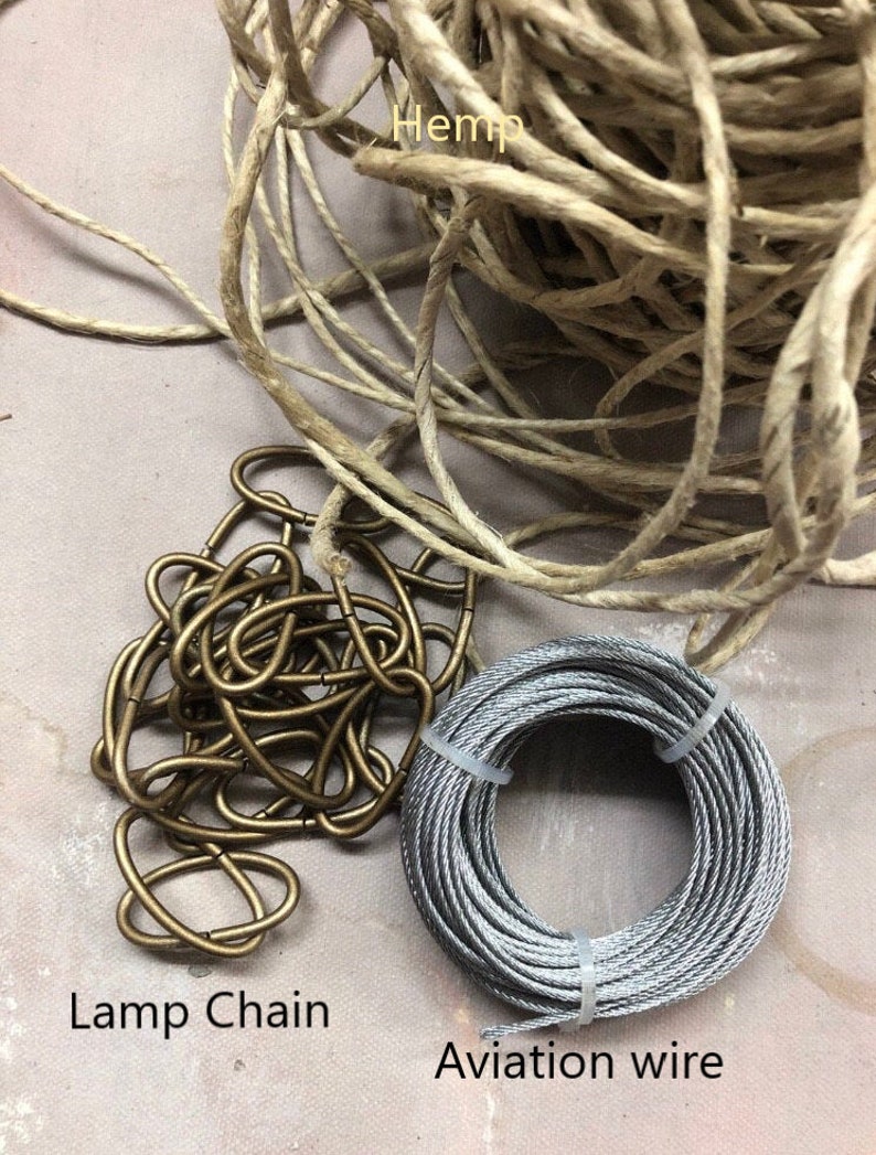 May include: A close-up of three different types of cord: hemp cord, lamp chain, and aviation wire. The hemp cord is a natural beige color, the lamp chain is gold, and the aviation wire is silver.
