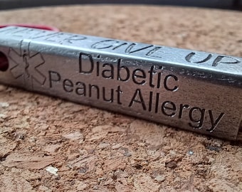 May include: A silver metal medical alert tag with a red lanyard. The tag features a red cross symbol and the text "Diabetic Peanut Allergy" engraved on it.