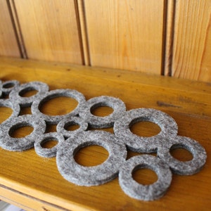 以下が含まれることがあります： 重なり合った円形のユニークなデザインが施されたグレーのフェルトコースター。コースターは柔らかく質感のある素材で作られており、熱や傷から表面を保護するのに最適です。