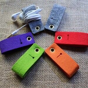 Puede incluir: Seis organizadores de cables de fieltro en diferentes colores, incluyendo gris, morado, verde, naranja y rojo. Cada organizador tiene un pequeño agujero para enhebrar los cables.