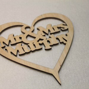 Puede incluir: Un adorno para pastel de madera en forma de coraz&oacute;n con el texto "Mr & Mrs Murphy" recortado.