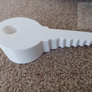 May include: A white key-shaped object with a textured surface and a circular hole. The key's head is rounded, and the teeth are clearly defined. The object is likely a decorative item or a prop.