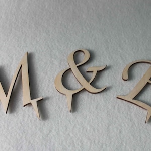 May include: Wooden letters spelling "M & E" in a cursive font. The letters are light brown and have a rustic look.