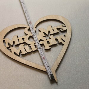 Puede incluir: Un letrero de madera en forma de coraz&oacute;n con el texto "Mr. & Mrs. Murphy" recortado. El letrero se est&aacute; midiendo con una regla.