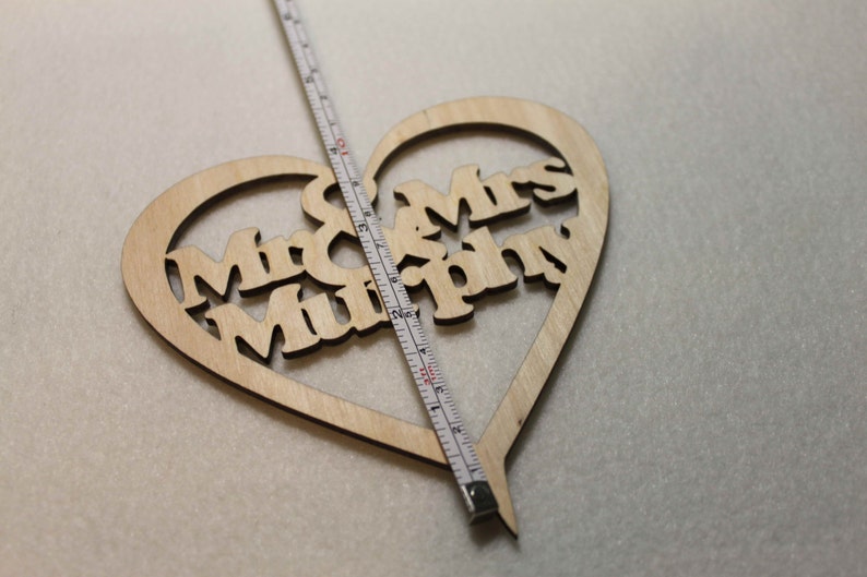 Puede incluir: Un letrero de madera en forma de coraz&oacute;n con el texto "Mr. & Mrs. Murphy" recortado. El letrero se est&aacute; midiendo con una regla.