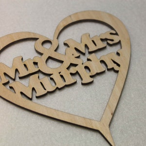 Puede incluir: Un adorno para pastel de madera en forma de coraz&oacute;n con el texto "Mr & Mrs Murphy" recortado.