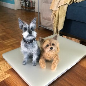 May include: Two felted dog figurines, one gray and one brown, sitting on a silver laptop.