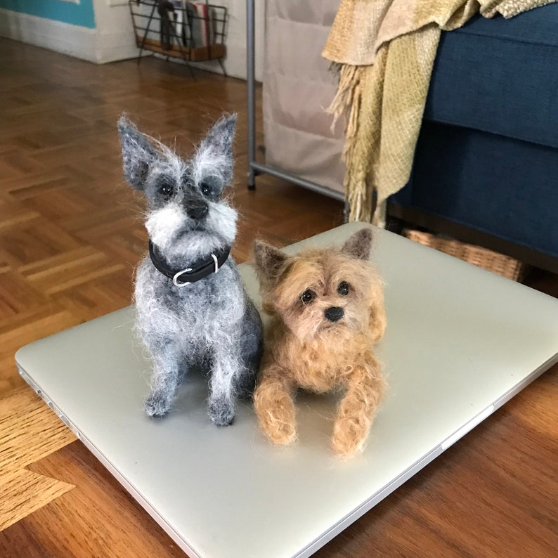 May include: Two felted dog figurines, one gray and one brown, sitting on a silver laptop.
