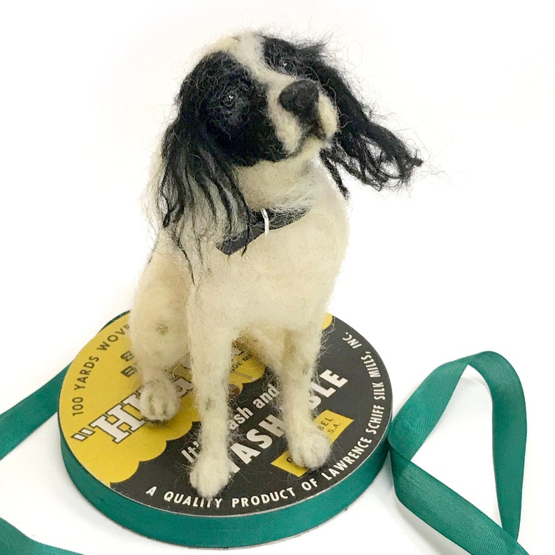 May include: A needle felted black and white dog figurine sitting on a spool of thread. The spool is labeled "100 Yards Woven", "H-Ash and Ashle", and "A Quality Product of Lawrence Schiff Silk Mills, Inc."