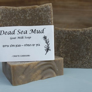 以下が含まれることがあります： 白いラベルに英語とヘブライ語で「Dead Sea Mud Goat Milk Soap」と書かれた、茶色の死海泥ヤギミルク石鹸が2本。ラベルには「CRAFTE CARAVAN」の文字も記載されています。
