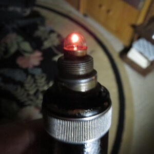 May include: A close-up of a black and silver medical device with a red light bulb at the top.