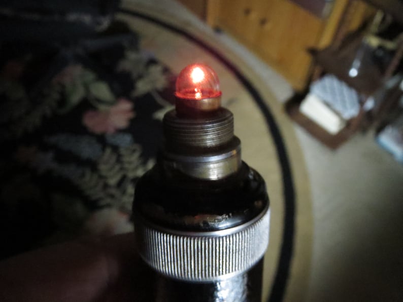 May include: A close-up of a black and silver medical device with a red light bulb at the top.