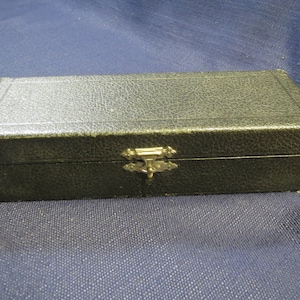 May include: A black rectangular box with a gold metal clasp. The box has a textured surface and is closed.