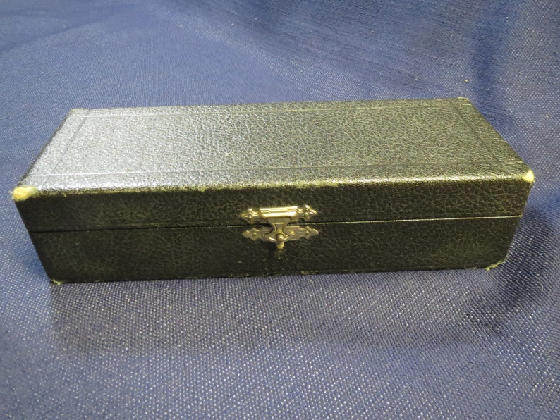 May include: A black rectangular box with a gold metal clasp. The box has a textured surface and is closed.