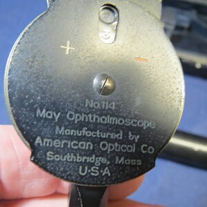 May include: A black metal May Ophthalmoscope, model No. 114, manufactured by American Optical Co. in Southbridge, Mass. USA.
