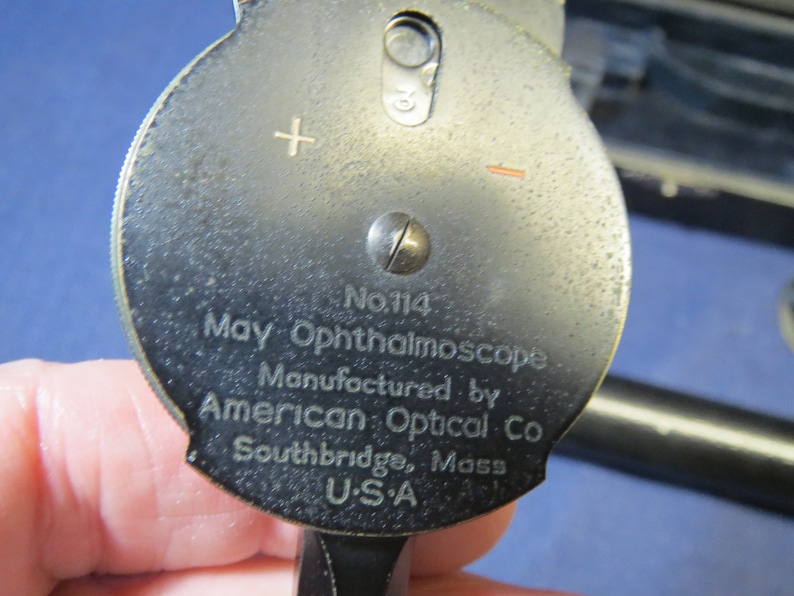May include: A black metal May Ophthalmoscope, model No. 114, manufactured by American Optical Co. in Southbridge, Mass. USA.