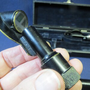 May include: A black metal medical instrument with a round lens and a knurled knob. The instrument is marked with the number "B 370".