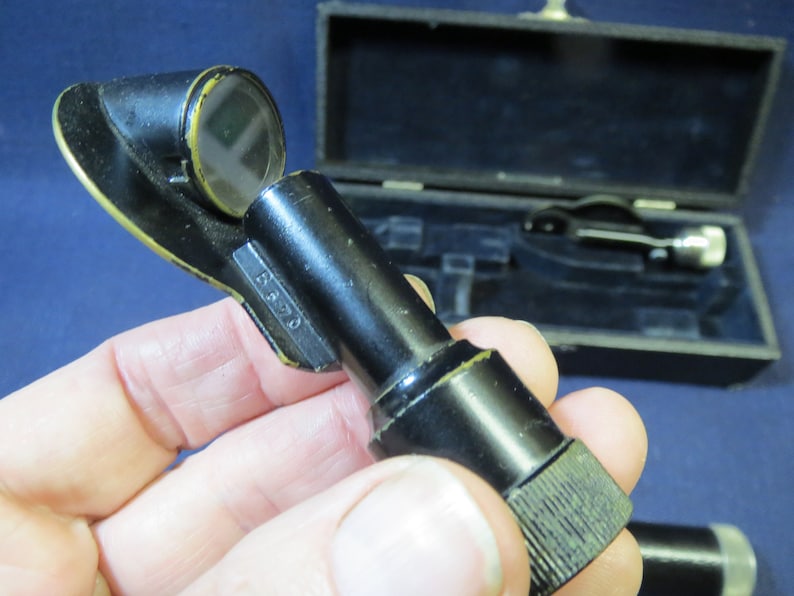 May include: A black metal medical instrument with a round lens and a knurled knob. The instrument is marked with the number "B 370".