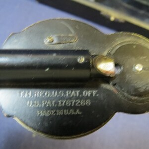 May include: Close-up of a black metal device with a silver tip and a round dial. The device has the text "T.M. REG. U.S. PAT. OFF. U.S. PAT. 1767268 MADE IN U.S.A." engraved on the side.