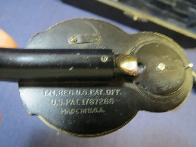 May include: Close-up of a black metal device with a silver tip and a round dial. The device has the text "T.M. REG. U.S. PAT. OFF. U.S. PAT. 1767268 MADE IN U.S.A." engraved on the side.