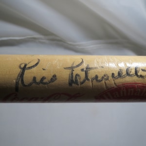 May include: A wooden baseball bat with a black signature that reads "Rico Petrocelli" on the barrel. The bat is also stamped with the words "Louisville Slugger" and "Official League Baseball" in red.