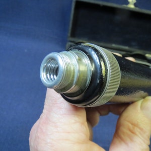 May include: Close-up of a black and silver medical instrument with a threaded end. The instrument is held in a hand.