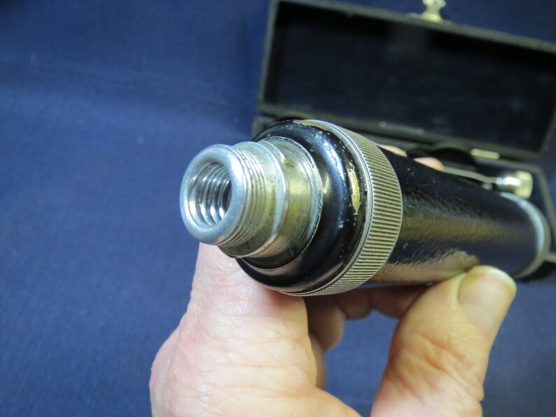 May include: Close-up of a black and silver medical instrument with a threaded end. The instrument is held in a hand.