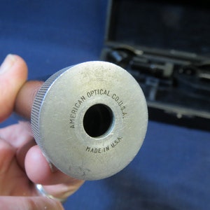 May include: Close-up of a silver metal tube with the text "AMERICAN OPTICAL CO. U.S.A." and "MADE IN U.S.A." engraved on the side.
