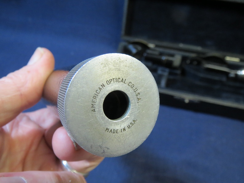 May include: Close-up of a silver metal tube with the text "AMERICAN OPTICAL CO. U.S.A." and "MADE IN U.S.A." engraved on the side.