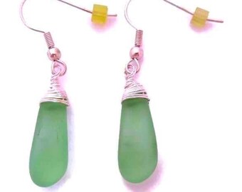May include: A pair of drop earrings featuring smooth, teardrop-shaped light green sea glass pendants. Each pendant is securely wrapped at the top with silver-toned wire, attached to a silver-toned hook finding with a small yellow bead accent.