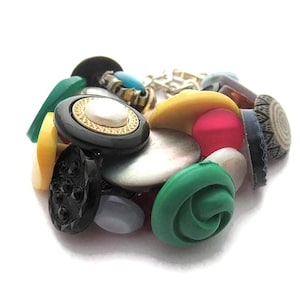 May include: A collection of colorful buttons in various shapes and sizes. The buttons include a variety of colors such as black, green, yellow, red, and white. Some buttons have decorative gold or silver accents.