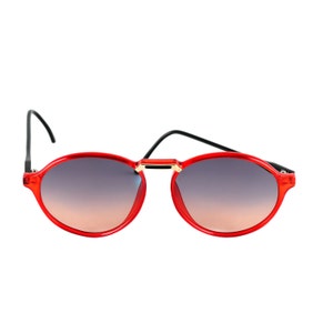 Puede incluir: Gafas de sol redondas rojas con patillas negras y puente dorado.