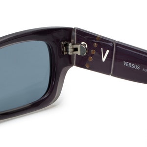 May include: Purple sunglasses with a silver hinge and the text "VERSUS MADE IN ITALY CE 2" on the arm.