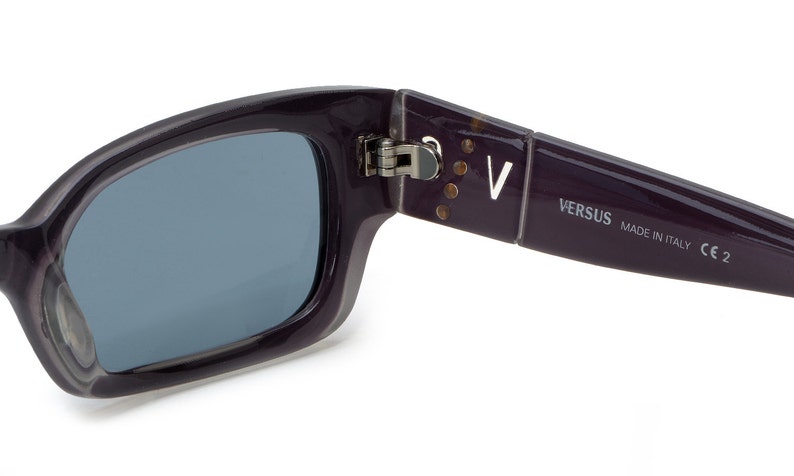 May include: Purple sunglasses with a silver hinge and the text "VERSUS MADE IN ITALY CE 2" on the arm.