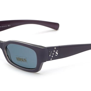 May include: Purple rectangular sunglasses with blue lenses. The sunglasses have a Versus Versace logo on the side.