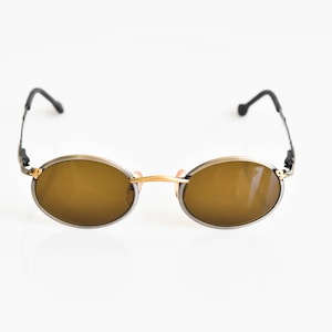 Puede incluir: Un par de gafas de sol ovaladas con montura de metal dorado y lentes marrones.