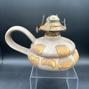May include: A ceramic oil lamp with a brown and yellow glaze. The lamp has a handle and a metal wick holder.