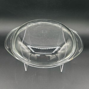 May include: A clear glass lid for a baking dish. The lid has a rounded edge and a flat top.