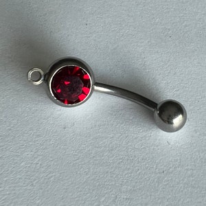 May include: A silver body piercing with a red gem in the centre. The piercing has a curved bar and a ball on the end.