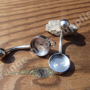 May include: Two silver belly button rings with round, flat, silver charms. The charms have a circular indentation in the center.