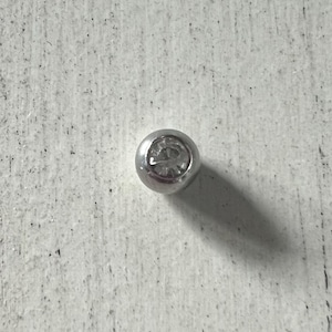 May include: A silver bead with a clear rhinestone in the center.