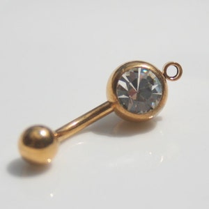May include: Gold body jewelry with a clear crystal and a small loop at the top.