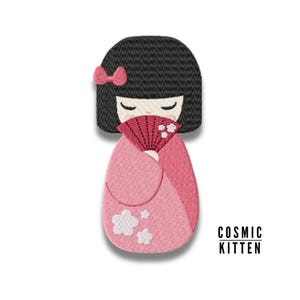 以下が含まれることがあります： ピンクの着物と白い花がついた赤い扇子を持った日本の女の子の人形を刺繍したパッチ。人形は黒髪でピンクのリボンをしています。