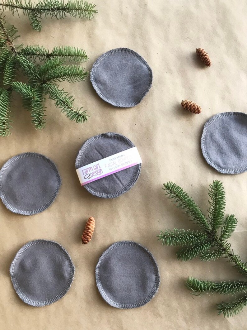May include: Six gray reusable makeup remover pads with a white label that reads "Farm Girl Design" and "Make-up Remover Pads". The pads are arranged in a circle on a brown paper background with pine branches and pine cones.