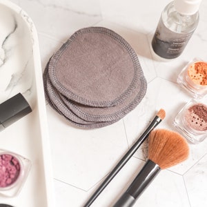 May include: A white marble tray with a variety of makeup products, including a lipstick, eyeshadow, and a bottle of makeup remover. There are also a set of gray reusable makeup remover pads and two makeup brushes.